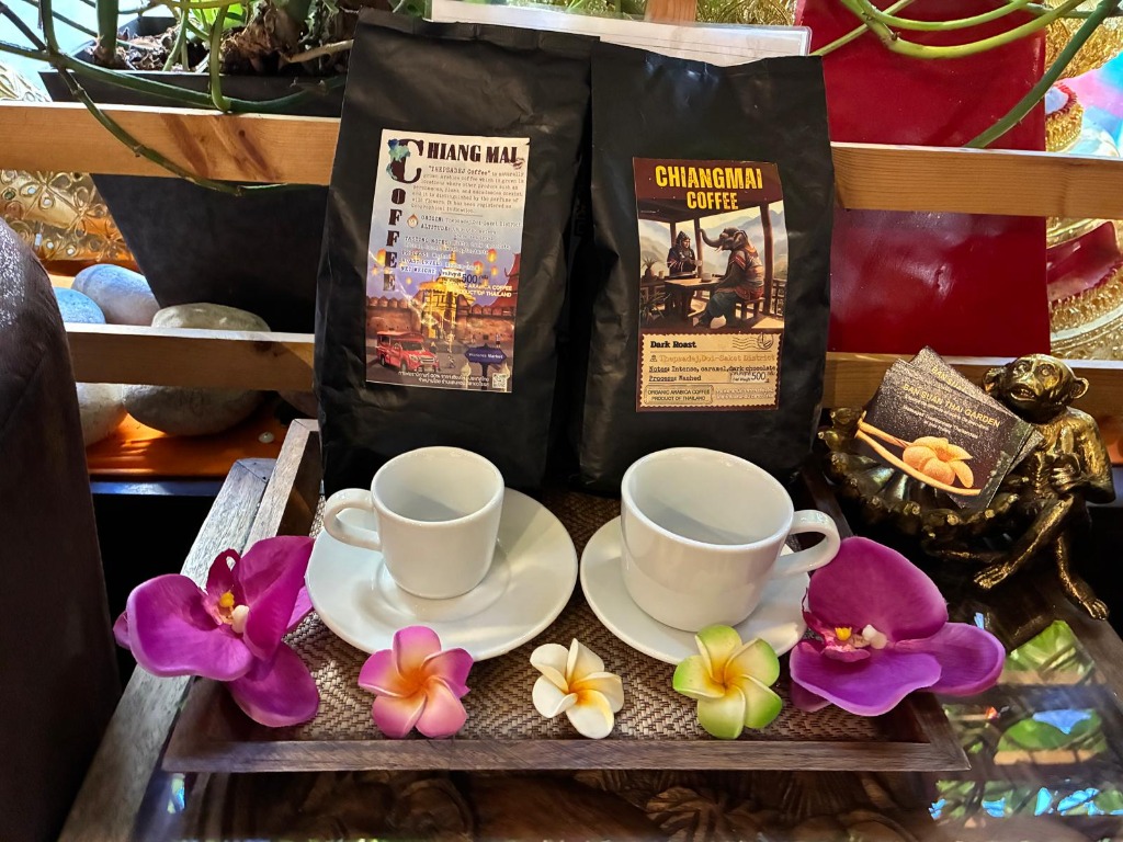 Deux tasses blanches sur un plateau décoré de fleurs, devant des sachets de café Chiang Mai.